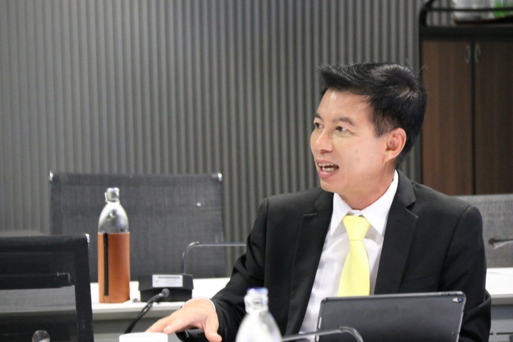 A person in a suit and tie sitting at a desk  Description automatically generated