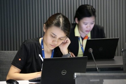 A group of people sitting at a table using a computer  Description automatically generated