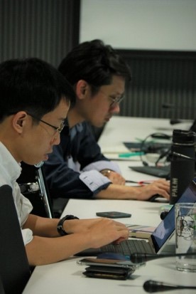 A group of people sitting at a desk looking at a computer  Description automatically generated